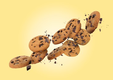 Image of Tasty chocolate chip cookies falling on light gold background