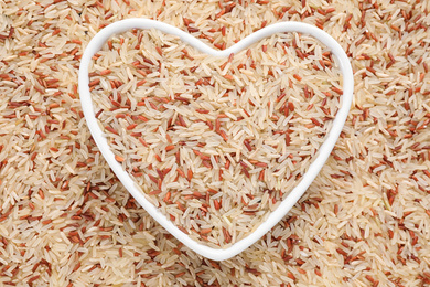 Photo of Mix of brown and polished rice with heart shaped bowl, top view
