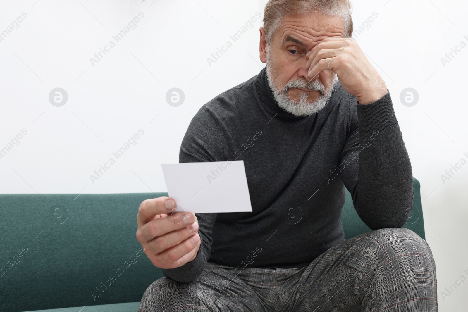 Photo of Upset senior man holding photo on sofa at home. Loneliness concept