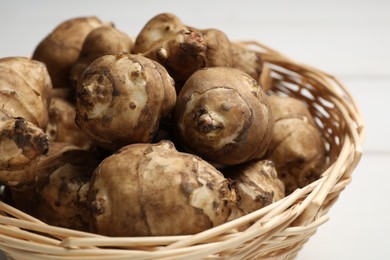 Wicker basket with fresh Jerusalem artichokes on white table, closeup