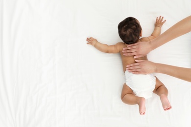 Photo of Top view of mother and her cute child on white bed, space for text. Baby massage and exercises