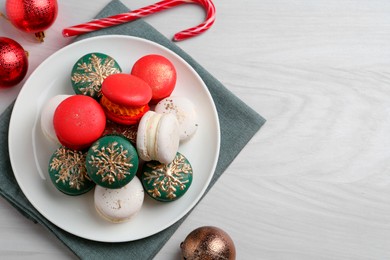 Different decorated Christmas macarons and festive decor on white wooden table, flat lay. Space for text