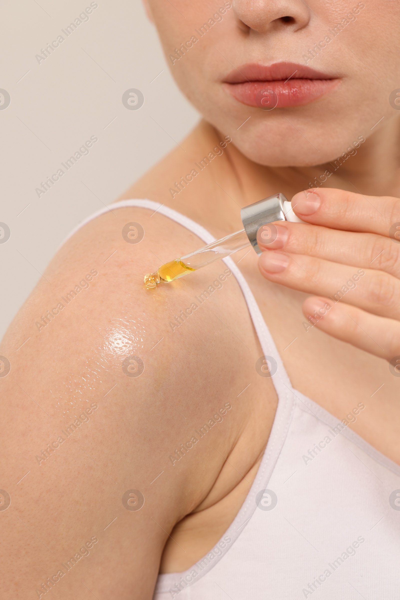 Photo of Woman applying essential oil onto shoulder on blurred background, closeup