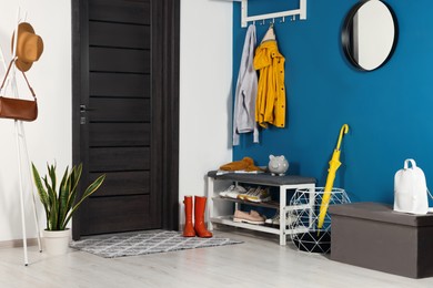 Photo of Stylish hallway with coat rack and shoe storage bench near blue wall. Interior design