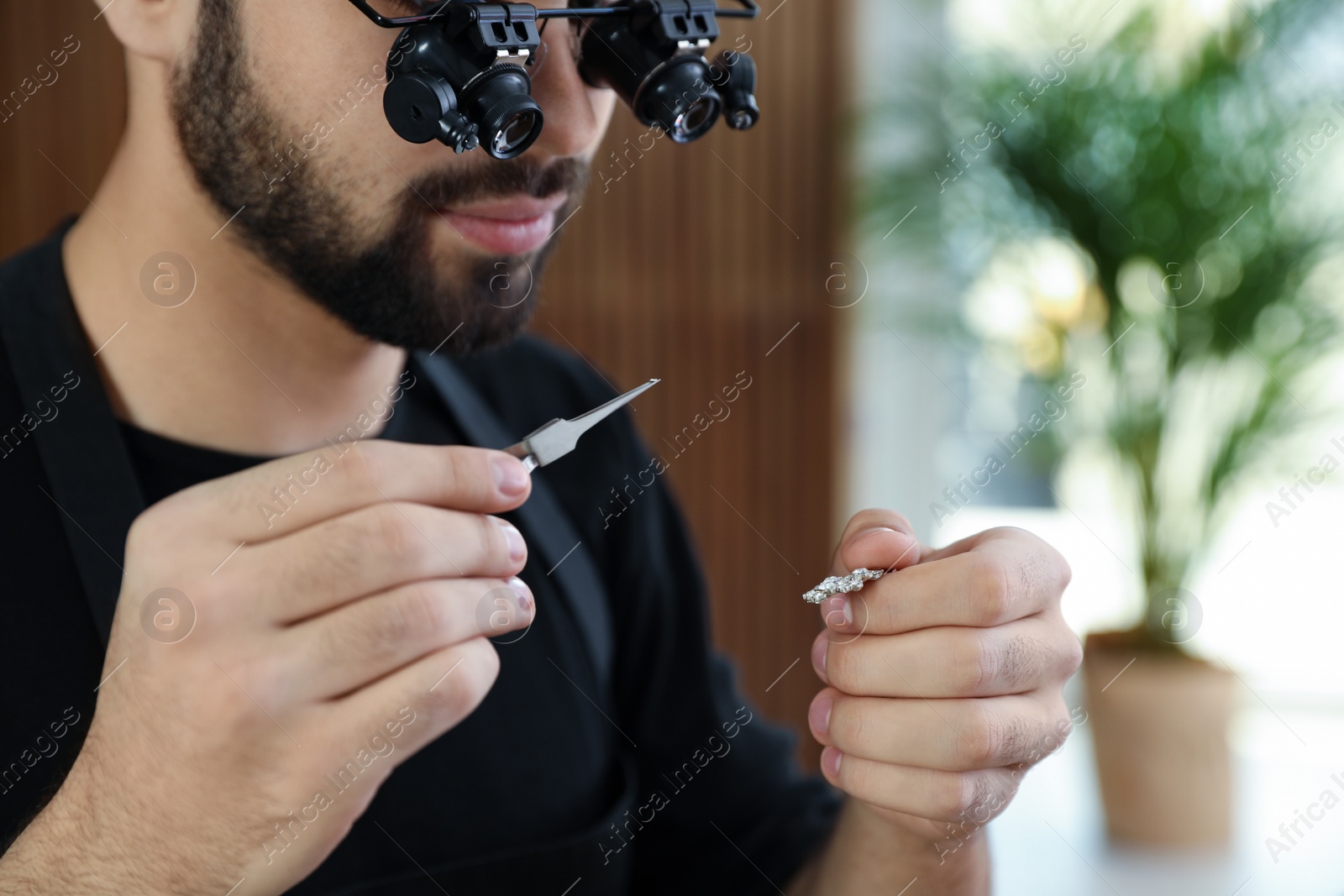 Photo of Male jeweler evaluating brooch in workshop, closeup