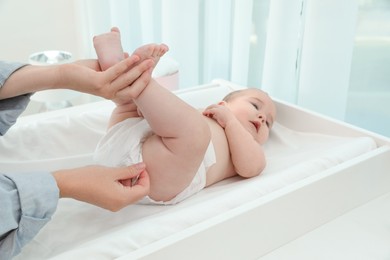 Mother changing baby's diaper at home, focus on hands