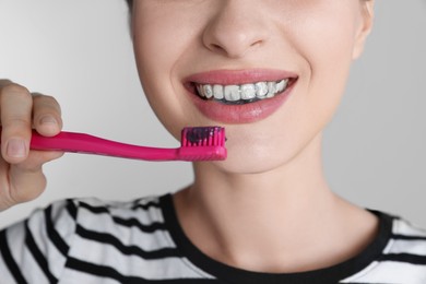 Photo of Woman brushing teeth with charcoal toothpaste on grey background, closeup