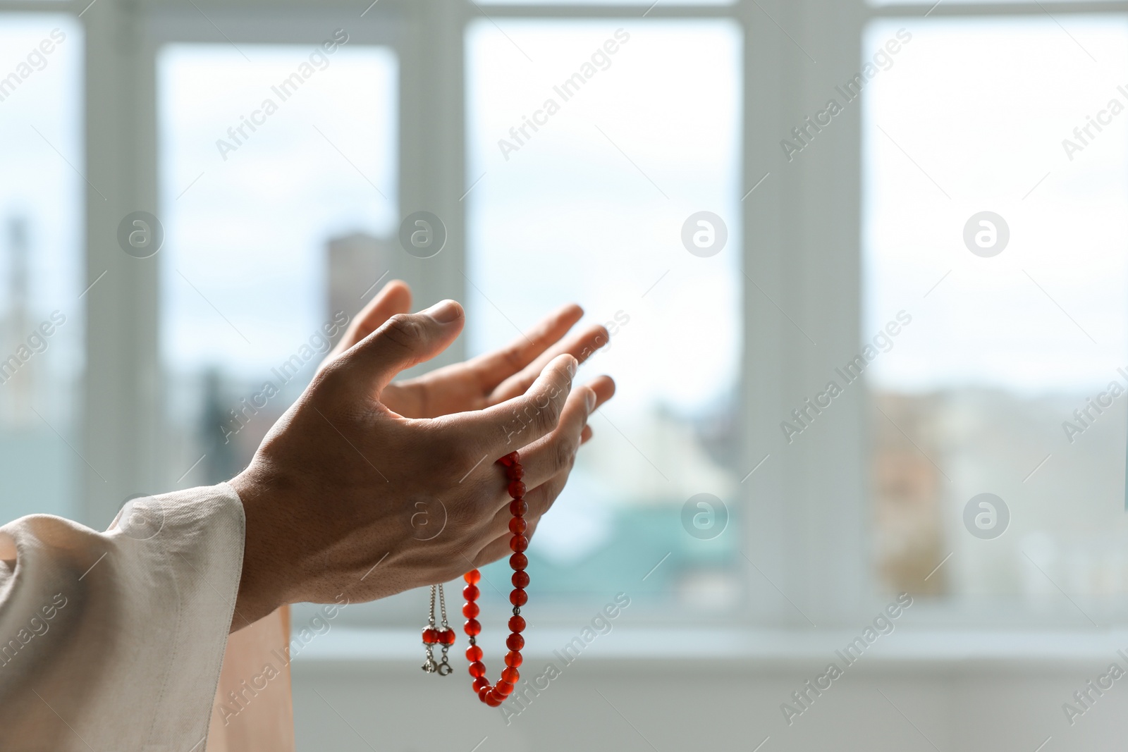 Photo of Muslim man with misbaha praying indoors, closeup. Space for text