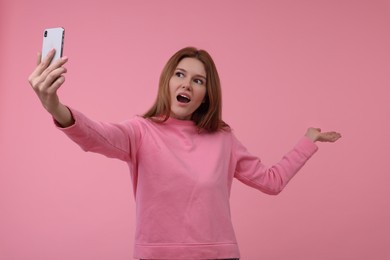 Beautiful woman taking selfie on pink background