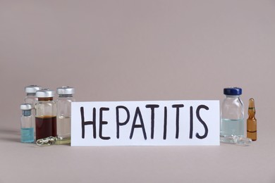 Word Hepatitis and vials with medicine on beige background