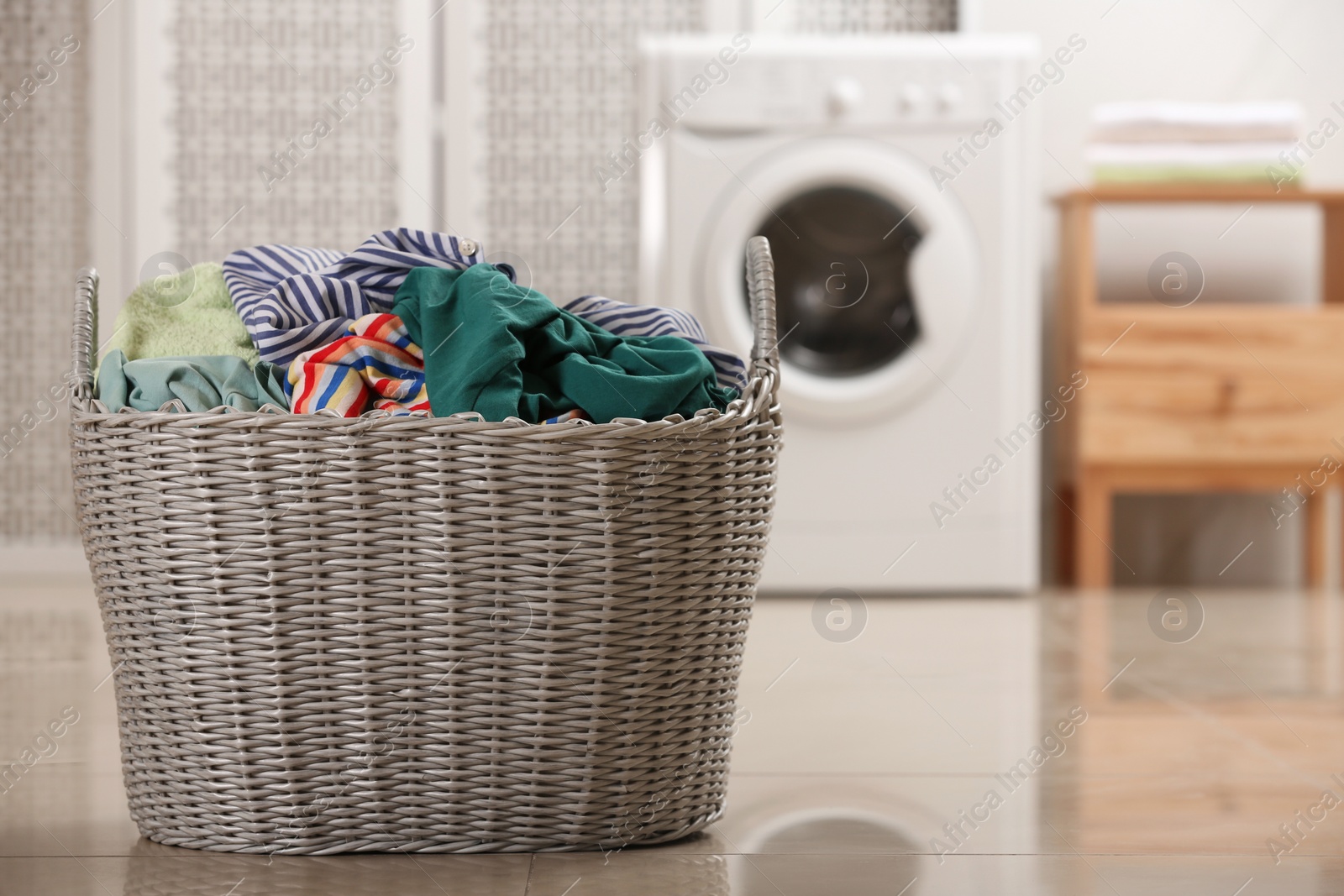 Photo of Wicker basket with dirty clothes on floor in laundry room, space for text