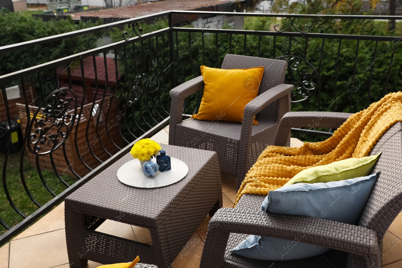 Photo of Colorful pillows, soft blanket and yellow chrysanthemum flowers on rattan garden furniture outdoors