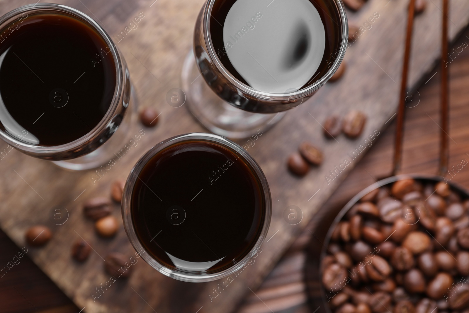 Photo of Shot glasses with coffee liqueur and beans on wooden table, top view