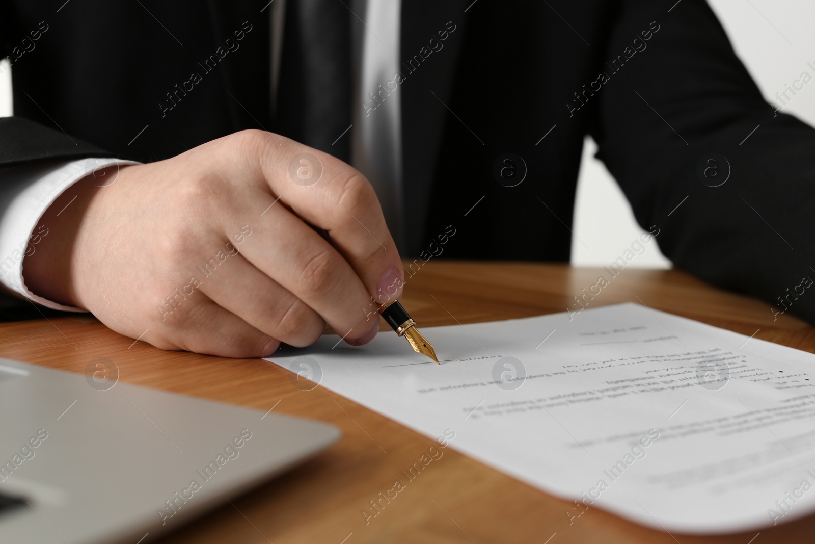 Photo of Notary signing document at wooden table, closeup