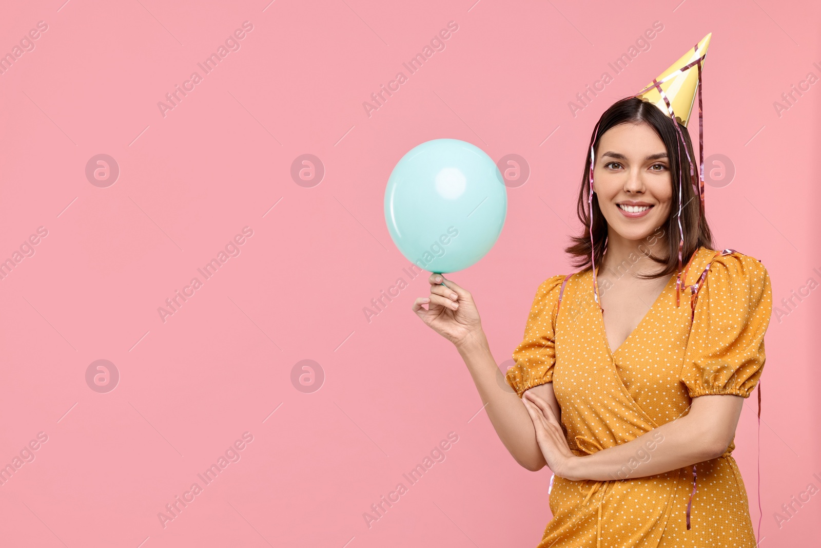 Photo of Happy young woman in party hat with balloon on pink background