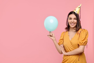 Happy young woman in party hat with balloon on pink background