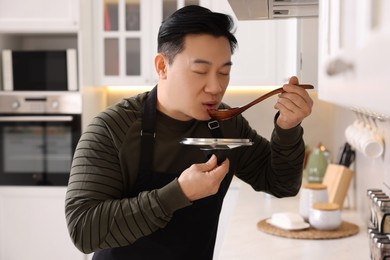 Photo of Cooking process. Man tasting dish in kitchen