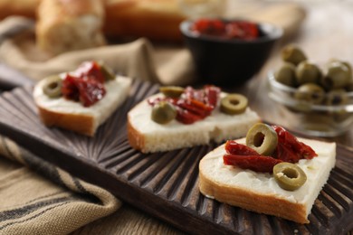 Delicious bruschettas with ricotta cheese, sun dried tomatoes and olives on table, closeup