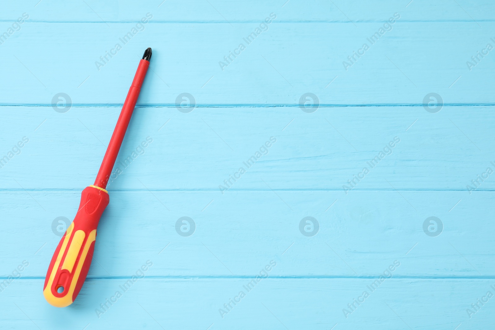 Photo of Screwdriver with red handle on light blue wooden table, top view. Space for text