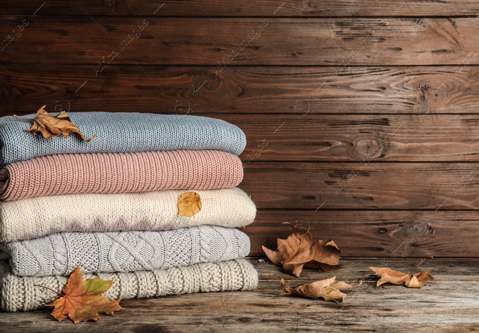 Photo of Stack of warm clothes with autumn leaves on wooden table. Space for text