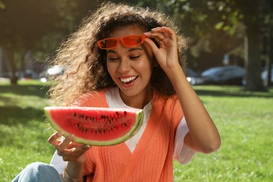 Photo of Beautiful young African American woman with slice of watermelon in park