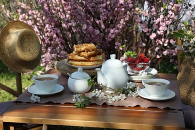 Photo of Beautiful spring flowers, freshly baked waffles and ripe strawberries on table served for tea drinking in garden