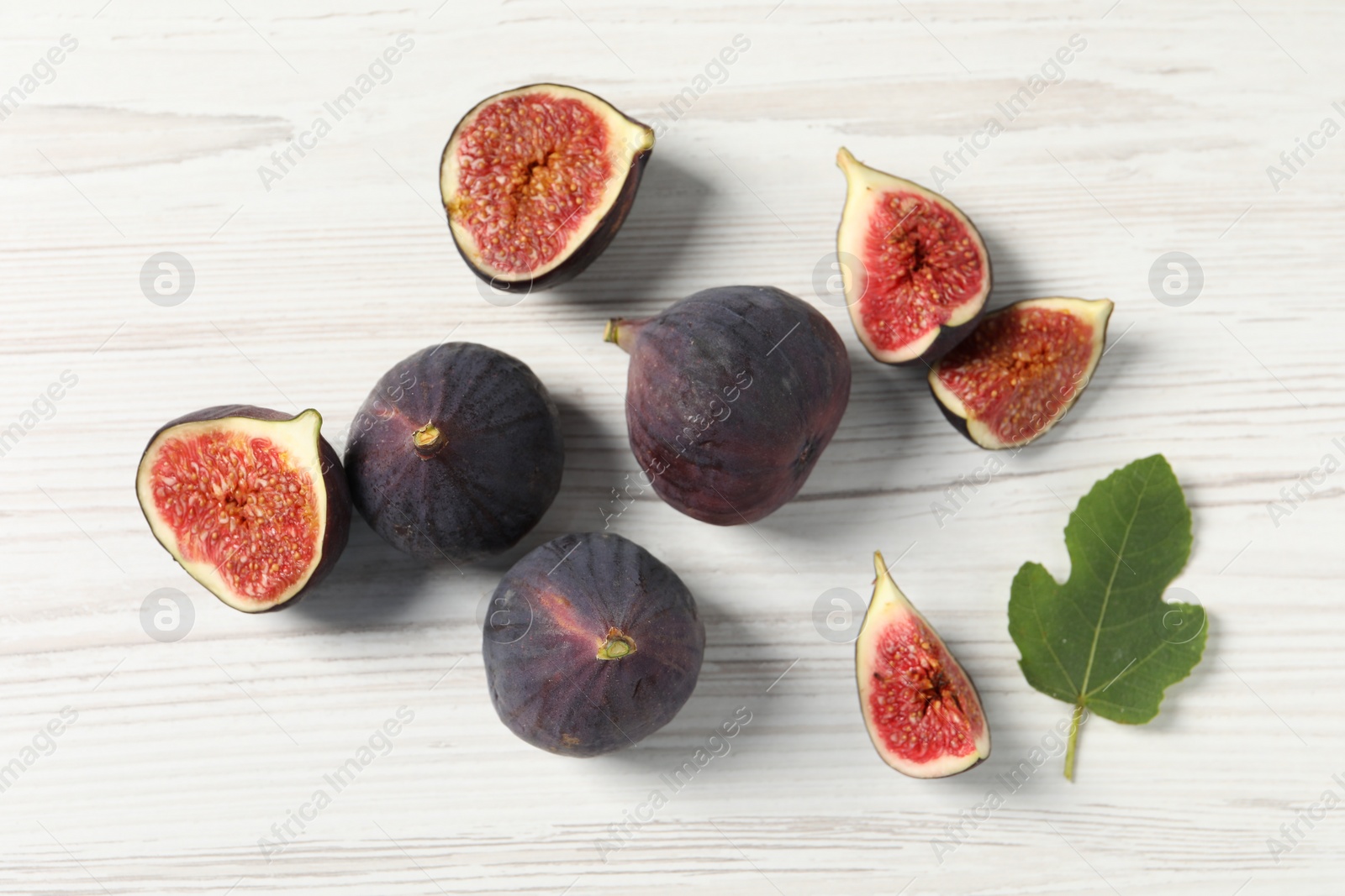 Photo of Whole and cut ripe figs with leaf on white wooden table, flat lay