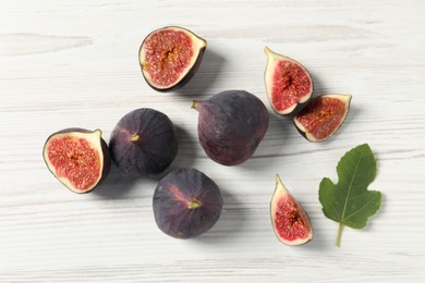 Whole and cut ripe figs with leaf on white wooden table, flat lay