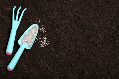 Photo of Flat lay composition with gardening tools and chemical fertilizer on soil. Space for text