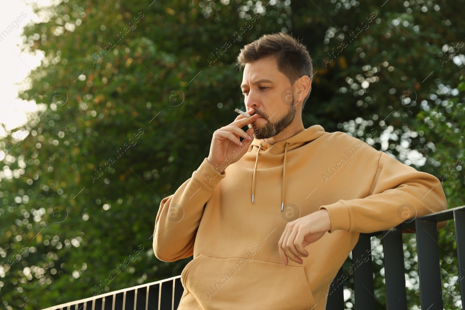 Photo of Man smoking cigarette near railing outdoors. Bad habit