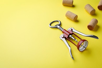 Photo of Corkscrew and wine bottle stoppers on yellow background. Space for text