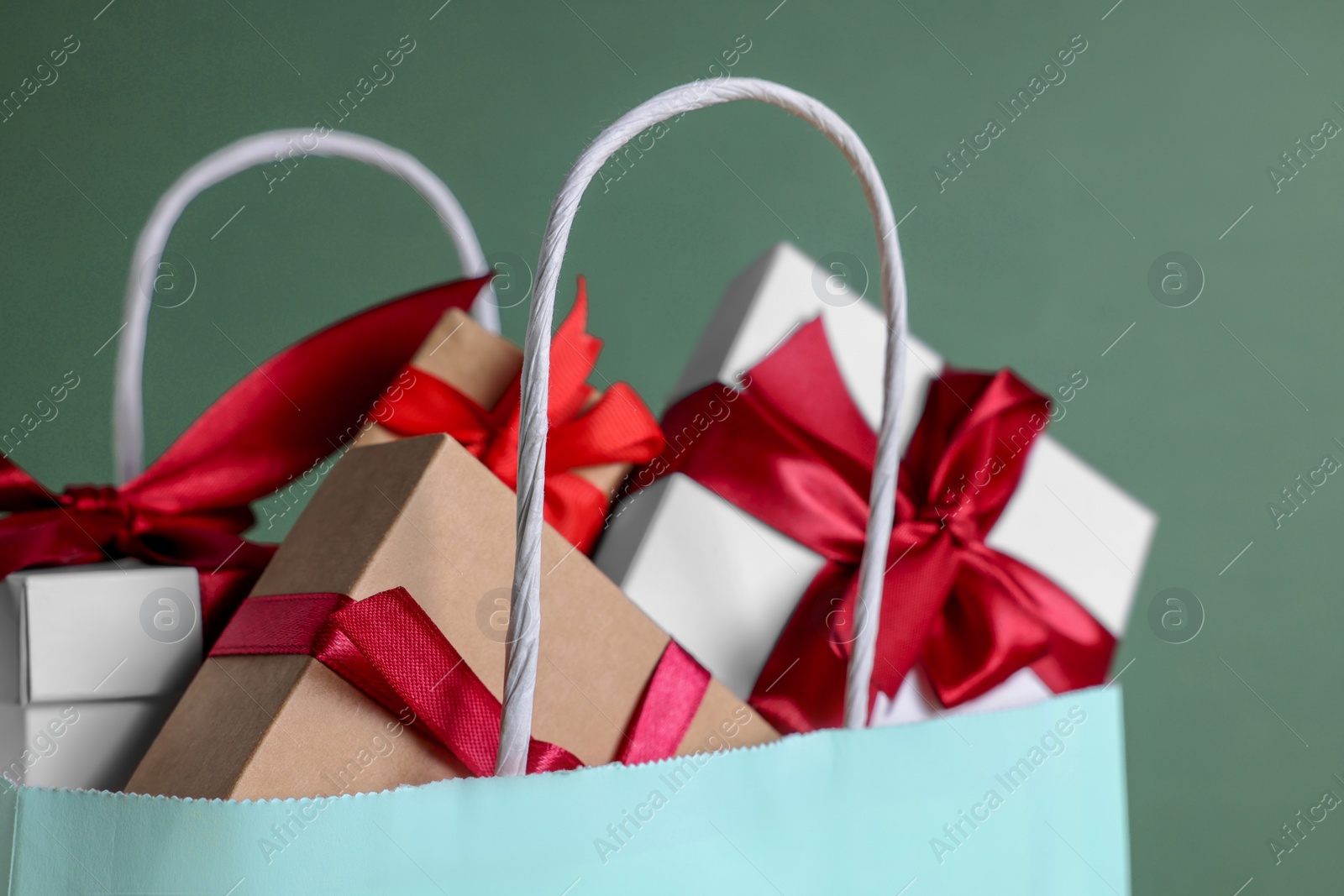 Photo of Turquoise paper shopping bag full of gift boxes on green background