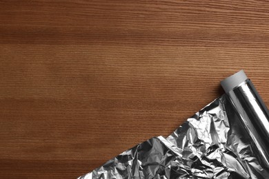 Photo of Roll of aluminum foil on wooden table, top view. Space for text