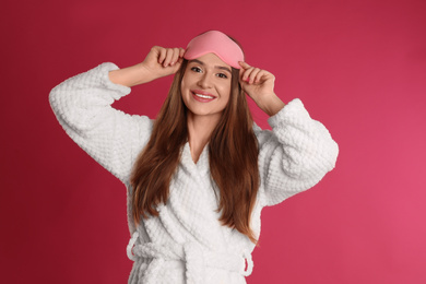 Young woman in bathrobe and eye sleeping mask on crimson background