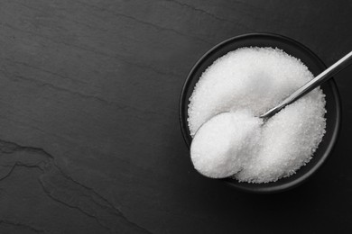 Photo of Granulated sugar and spoon in bowl on black table, top view. Space for text