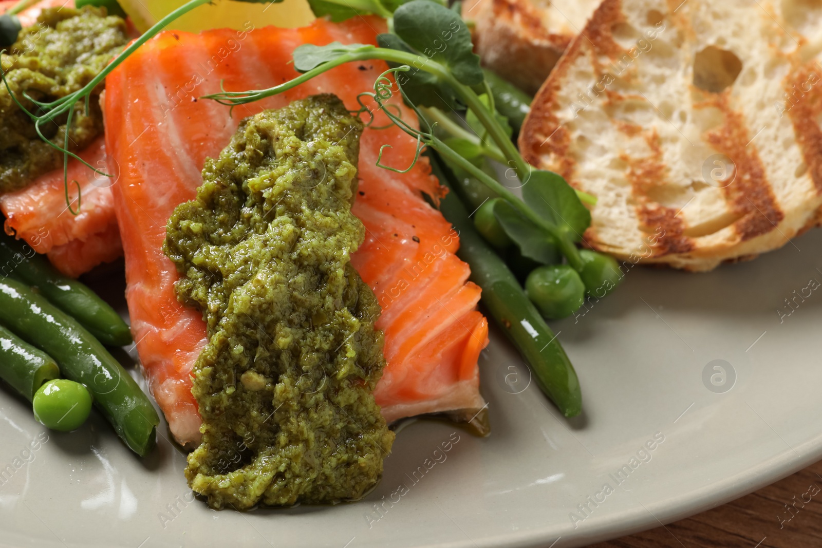 Photo of Tasty cooked salmon with pesto sauce served on plate, closeup