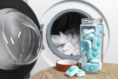 Photo of Jar with water softener tablets on wooden table near washing machine, space for text