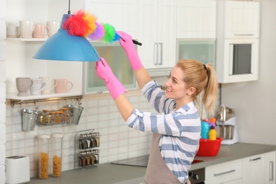Photo of Woman cleaning lamp with dust brush in kitchen