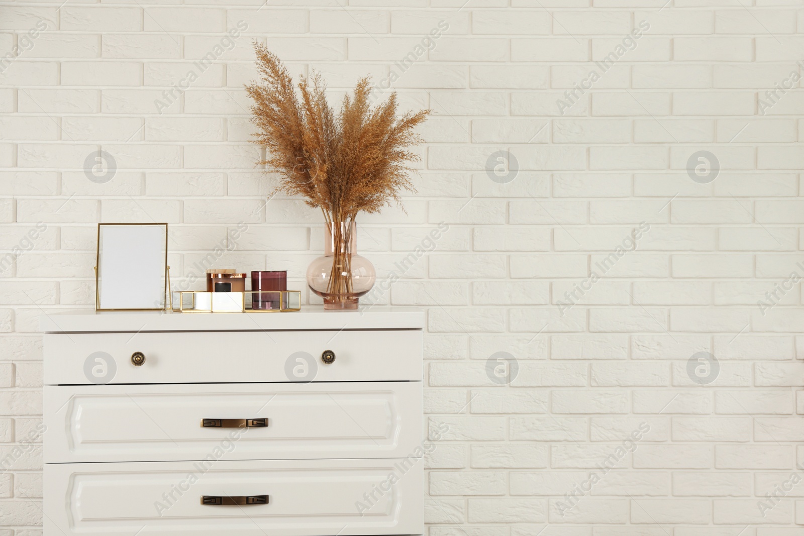 Photo of Modern chest of drawers with decor near white brick wall. Space for text