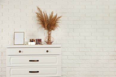 Modern chest of drawers with decor near white brick wall. Space for text