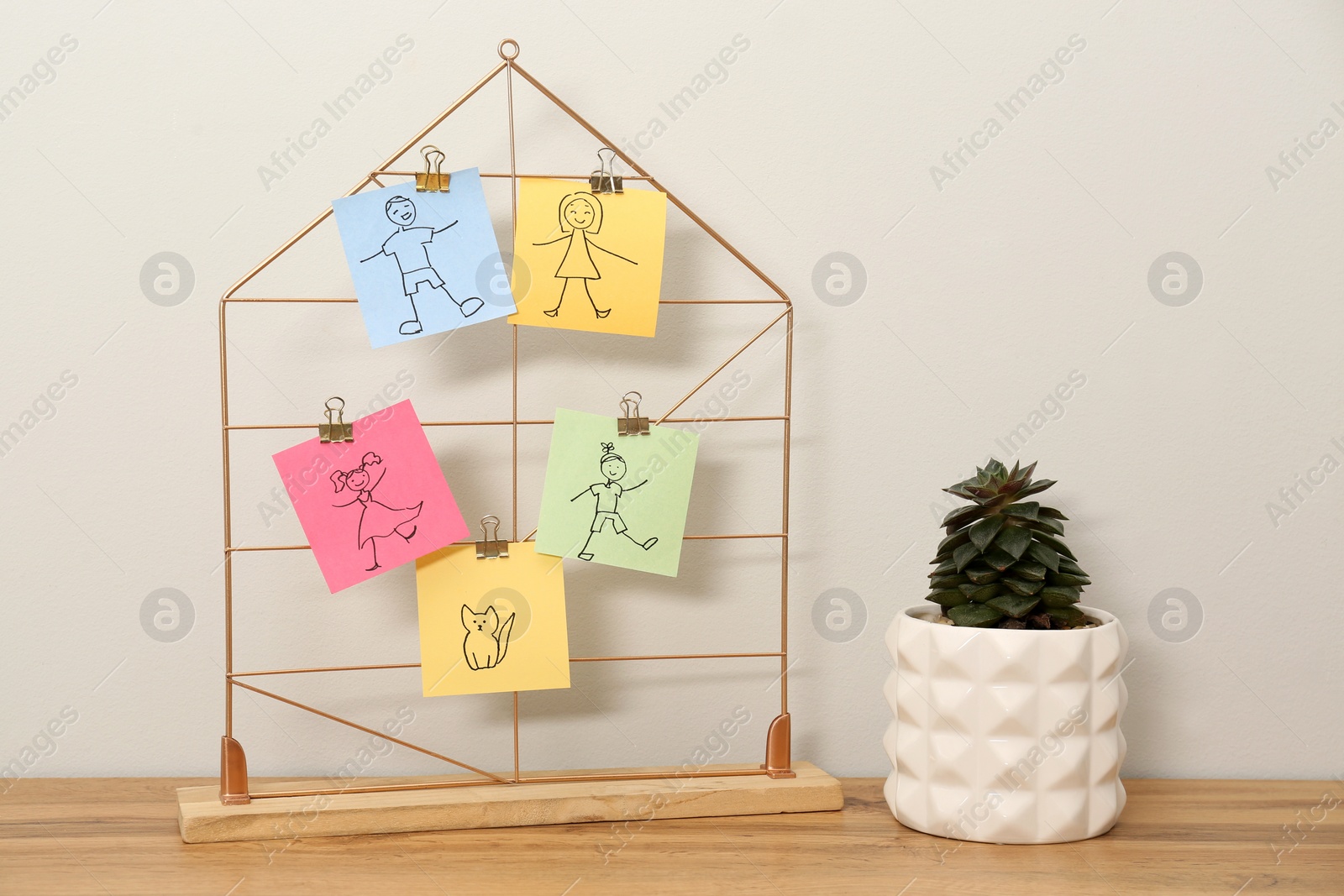 Photo of Pictures of family members attached to decorative house near plant on wooden table