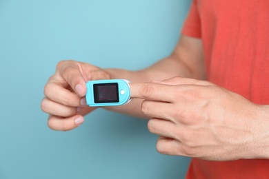 Photo of Young man checking pulse with blood pressure monitor on finger against color background, closeup