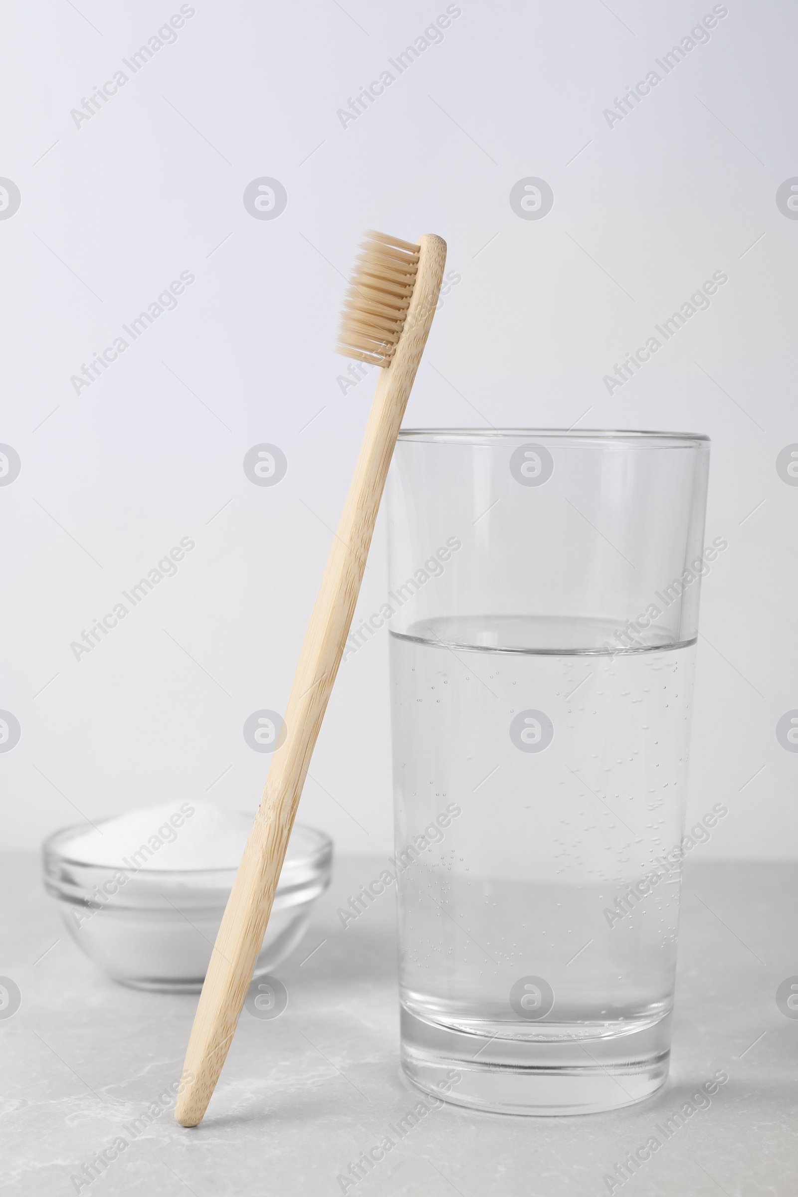 Photo of Bamboo toothbrush, bowl of baking soda and glass of water on light grey marble table