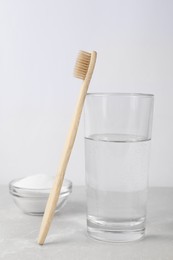 Bamboo toothbrush, bowl of baking soda and glass of water on light grey marble table