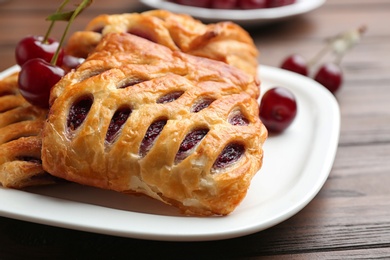 Fresh delicious puff pastry with sweet cherries served on wooden table, closeup