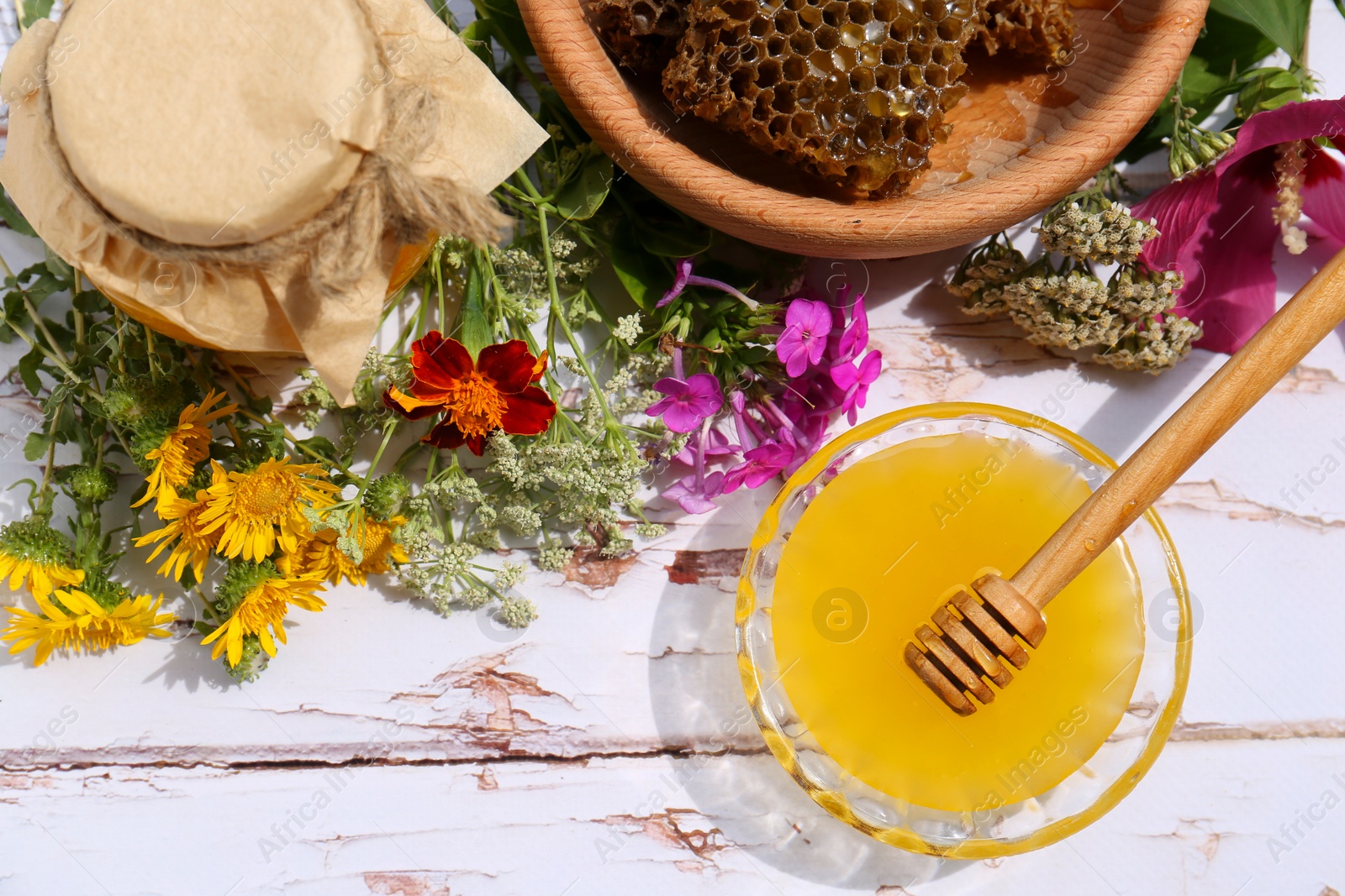 Photo of Delicious honey, combs and different flowers on white wooden table, flat lay