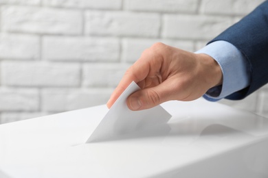 Man putting his vote into ballot box against brick wall, closeup