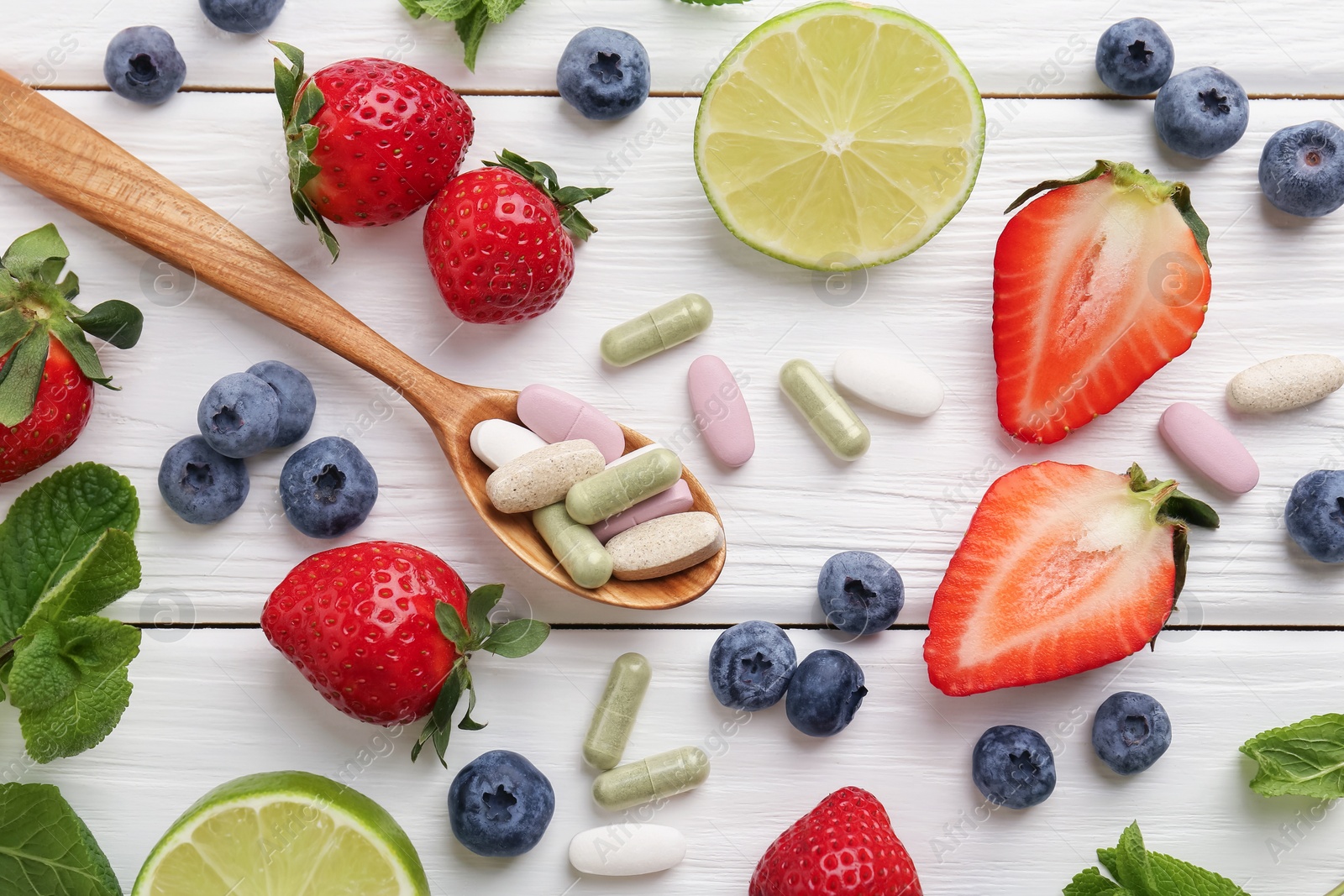 Photo of Different vitamin pills in spoon and fresh fruits on white wooden table, flat lay