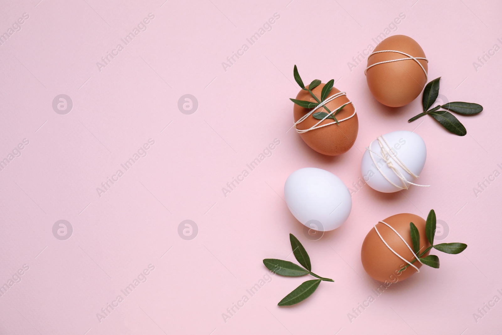 Photo of Beautifully decorated Easter eggs and green leaves on pale pink background, flat lay. Space for text