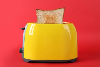 Photo of Modern toaster with slice of bread on red background